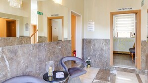 A reception area with marble flooring, two grey upholstered chairs, a small table with a candle and papers, and a chandelier. - Apartment in Oberhausen Near Ski Resort (Oberhausen)