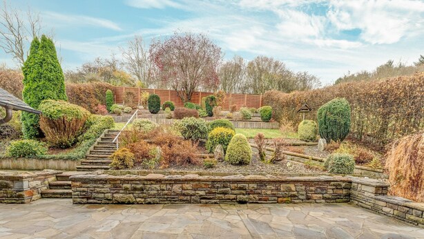 A stone patio with a wooden deck, surrounded by a landscaped garden with various shrubs and a wooden fence. - Spacious Flat in Adenau Near the Nurburgring (Adenau)