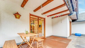 A wooden deck with a table and benches, a potted plant, and a view of a garden through a glass door. - Spacious Flat in Adenau Near the Nurburgring (Adenau)