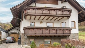 A two-story chalet with a wooden balcony, stone facade, and a car parked in front. - Spacious Flat in Adenau Near the Nurburgring (Adenau)