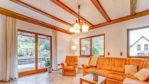 A living room with a sofa, armchair, and coffee table. There are large windows and a view of the outdoors. - Spacious Flat in Adenau Near the Nurburgring (Adenau)