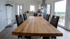 Uma cozinha moderna com armários brancos, uma geladeira de aço inoxidável e um espaço de jantar com mesa e cadeiras de madeira.