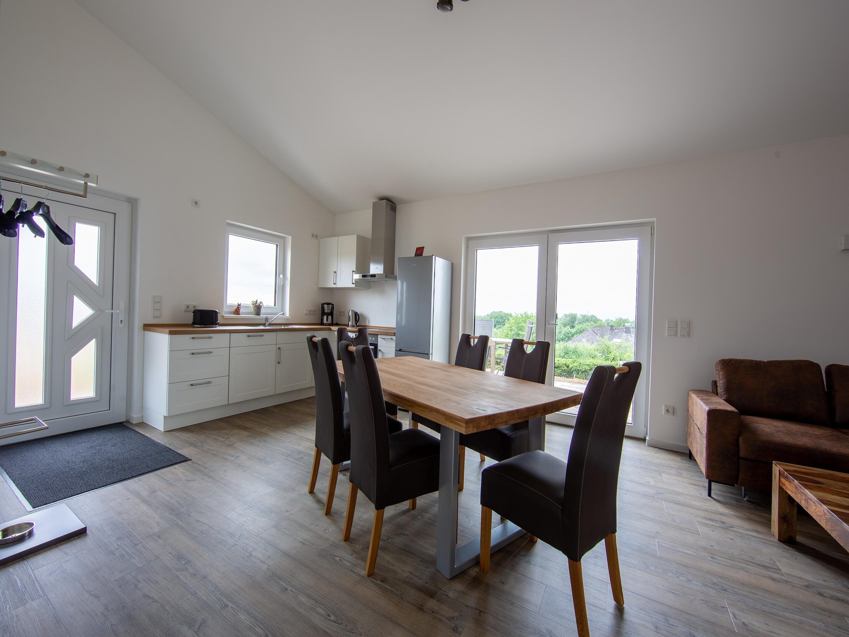 A modern kitchen with white cabinets, a wooden dining table, and a brown sofa.