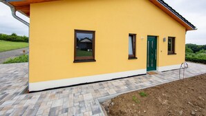 Um edifício amarelo com telhado em telhas, porta verde e duas janelas.