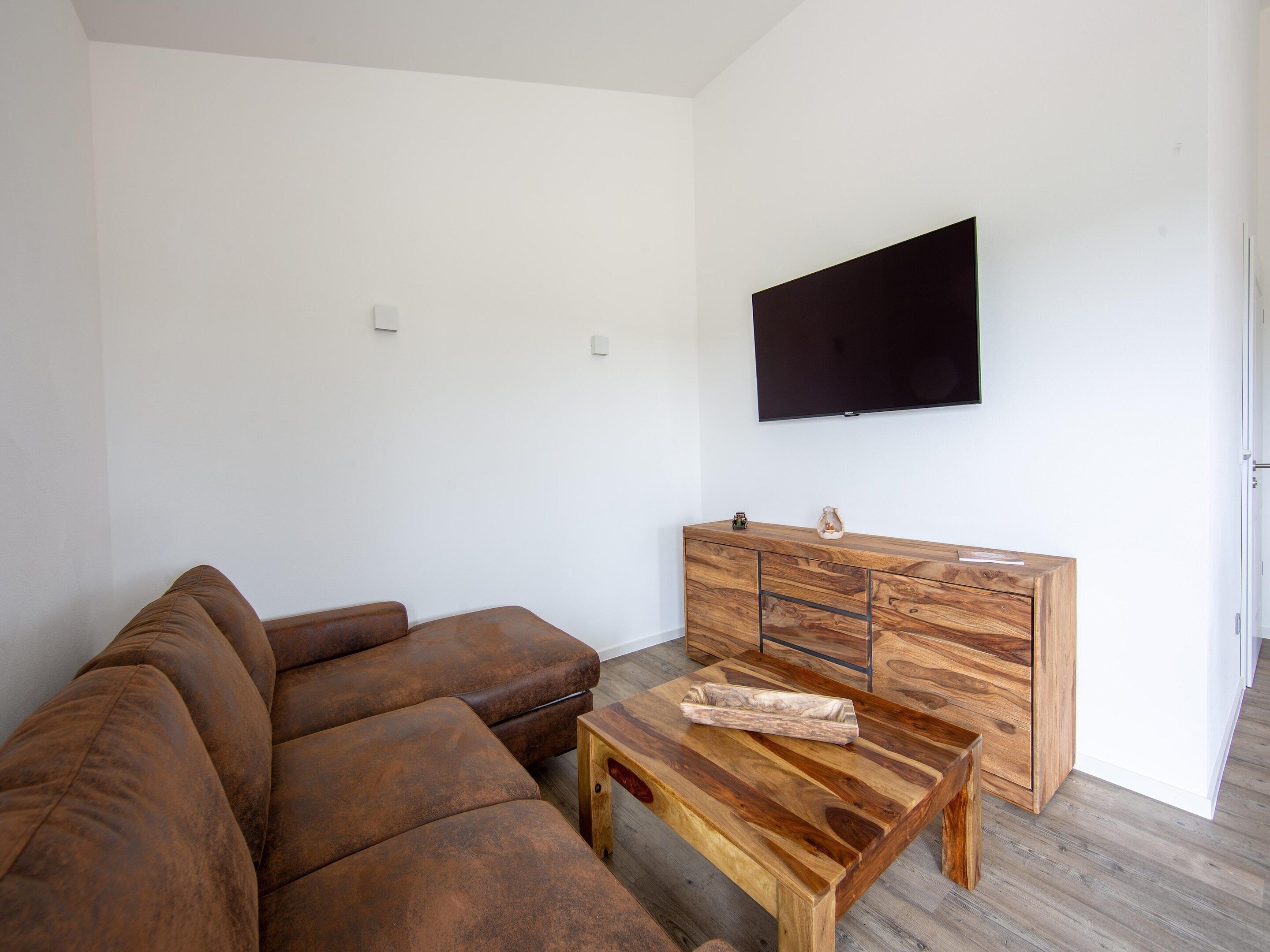 Een woonkamer met een bruine leren bank, een houten salontafel en een kast met een flatscreen televisie aan de muur.