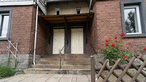 A brick building with two white doors, a wooden fence, and red flowers. - Holiday Home With Garden (Rechenberg-Bienenmuehle)