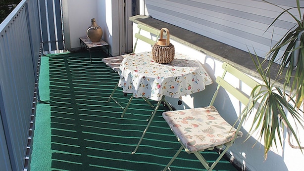 A balcony with a green striped floor, a small table with a floral tablecloth, a wicker lantern, and a chair with a floral cushion. - Wohnung im Teutoburger Wald (Blomberg)