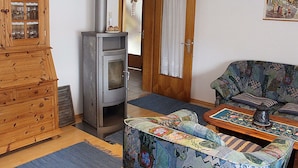A living room with a wood-burning stove, a wooden cabinet, a patterned sofa, and a door leading to another room. - Wohnung im Teutoburger Wald (Blomberg)