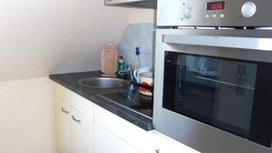 Et køkken med en rustfris stål ovn, et digitalt ur der viser 18:56, en vask og lyse skabe.