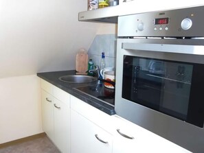 Modern kitchen with stainless steel oven, microwave, and sink, featuring white cabinetry and a wooden cutting board.