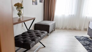 A modern living room with a tufted sofa, a small table with a vase of flowers, a grey ottoman, and a grey sofa. - Lakeside Base in Oberhausen (Oberhausen)