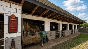 Une étable avec des bottes de foin, un tracteur vert et un panneau indiquant les noms des chevaux.
