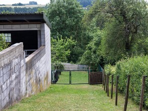 A fenced area with a building, a grassy path, and dense trees in the background.