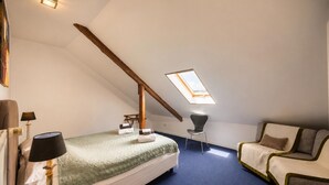 Une chambre avec un plafond en pente, un puits de lumière, un lit, une chaise et une lampe.