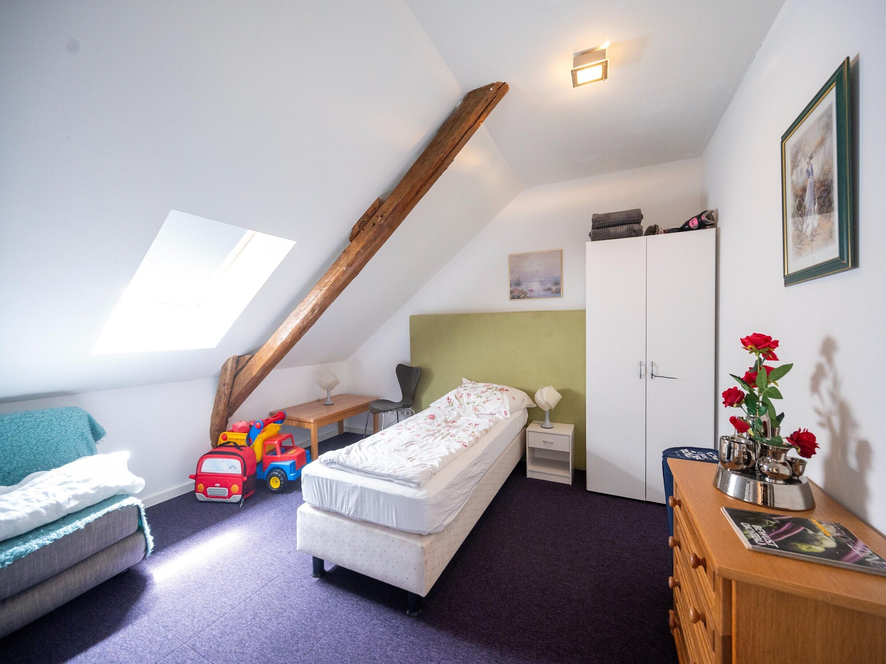A child's bedroom with a loft bed, a desk, a chair, a toy car, and a dresser with a vase of flowers.
