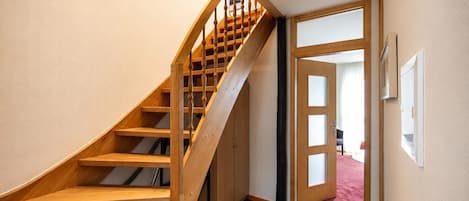A wooden staircase leading to a room with a door, a wall-mounted picture, and a tiled floor.