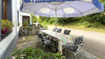 Un área de comedor al aire libre con mesa y sillas bajo un gran paraguas que dice 'Maisel's Weisse'.
