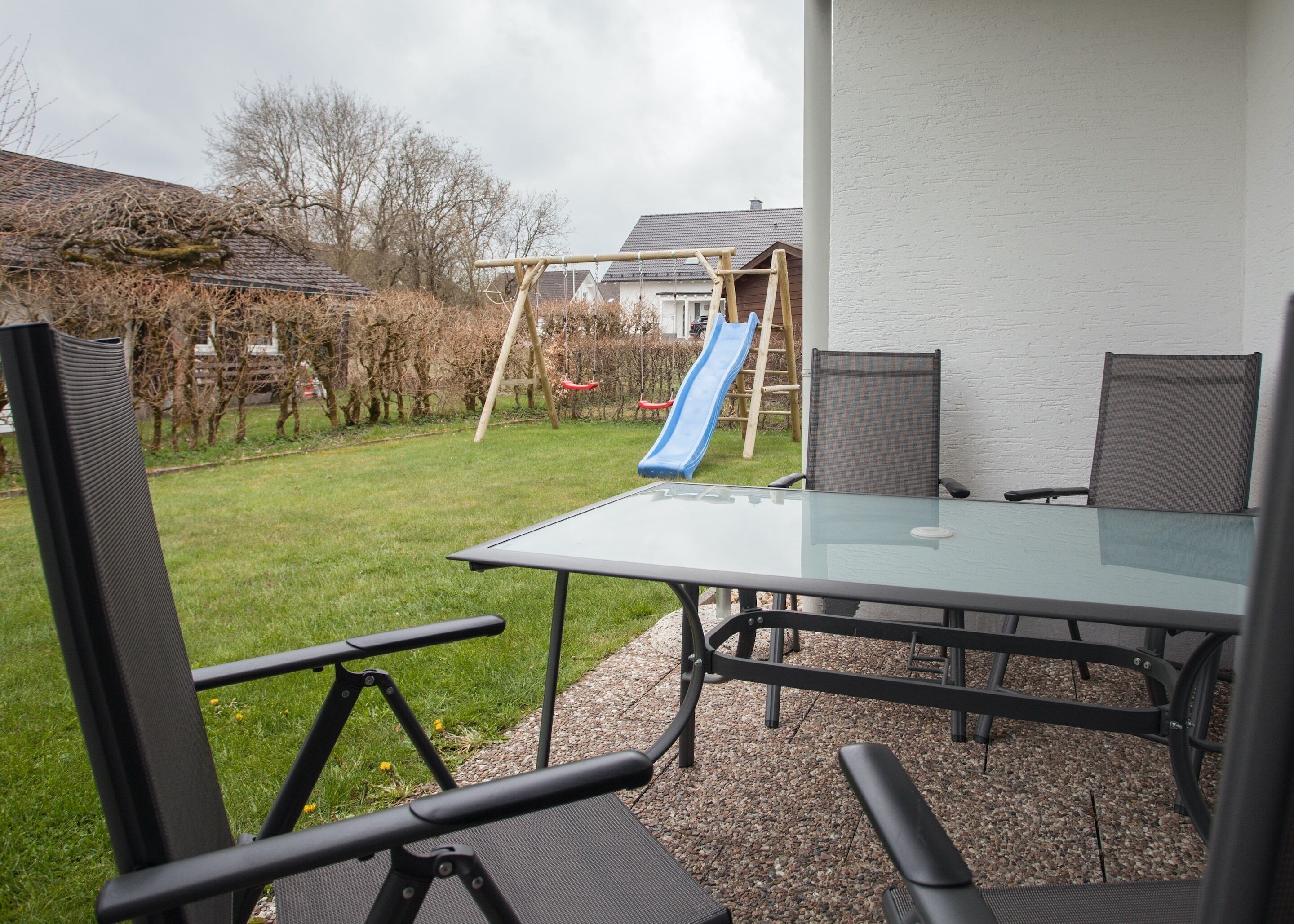 A patio with a glass table and chairs, a slide, and a wooden play structure.
