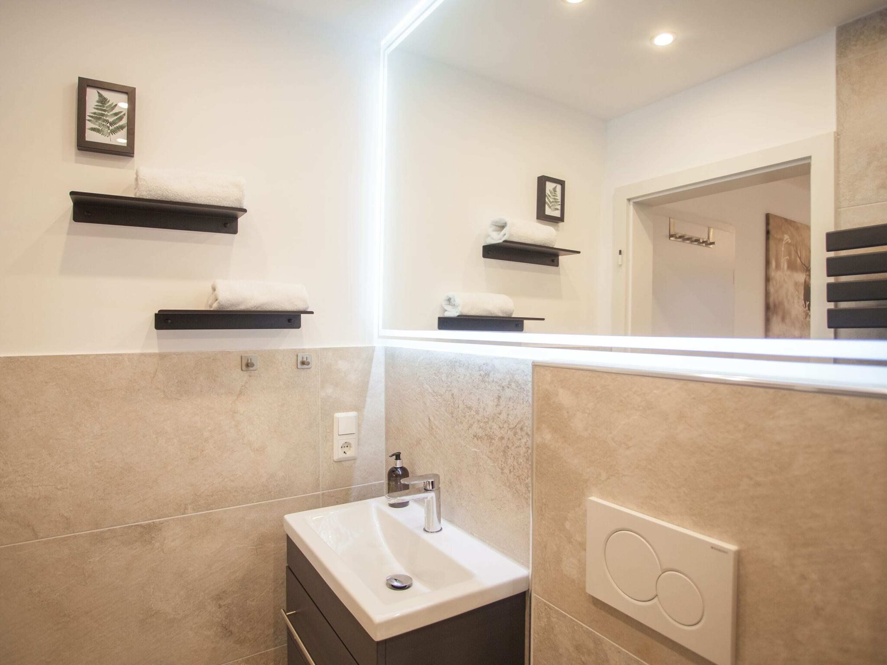 Een moderne badkamer met een witte wastafel, een spiegel en twee handdoekrekken aan de muur.