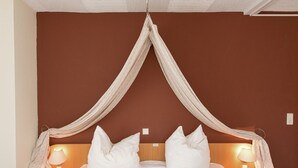 Een tweepersoonsbed met witte lakens, twee bedlampjes en een houten hoofdbord.