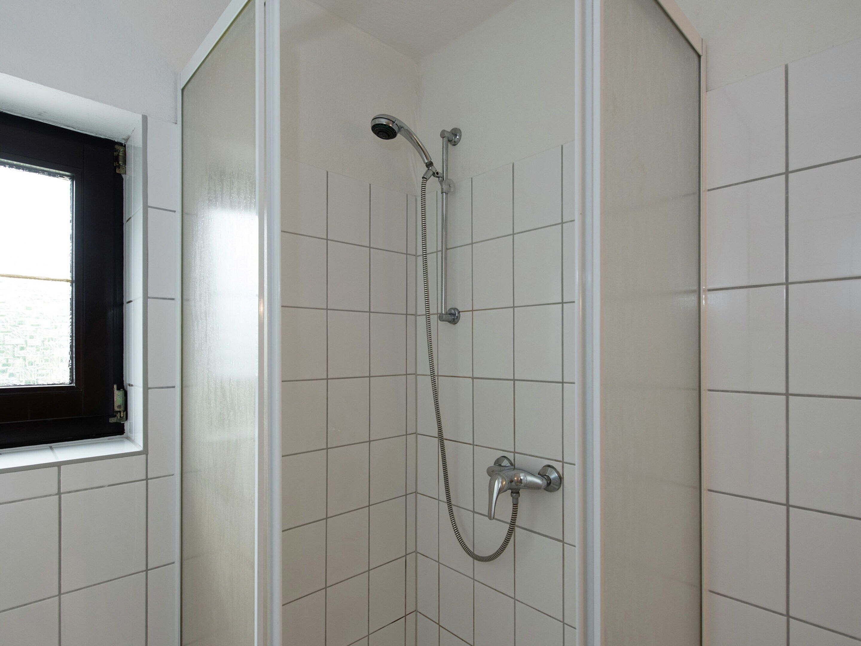 Une douche équipée d’un pommeau de douche à main et d’un robinet fixé au mur.