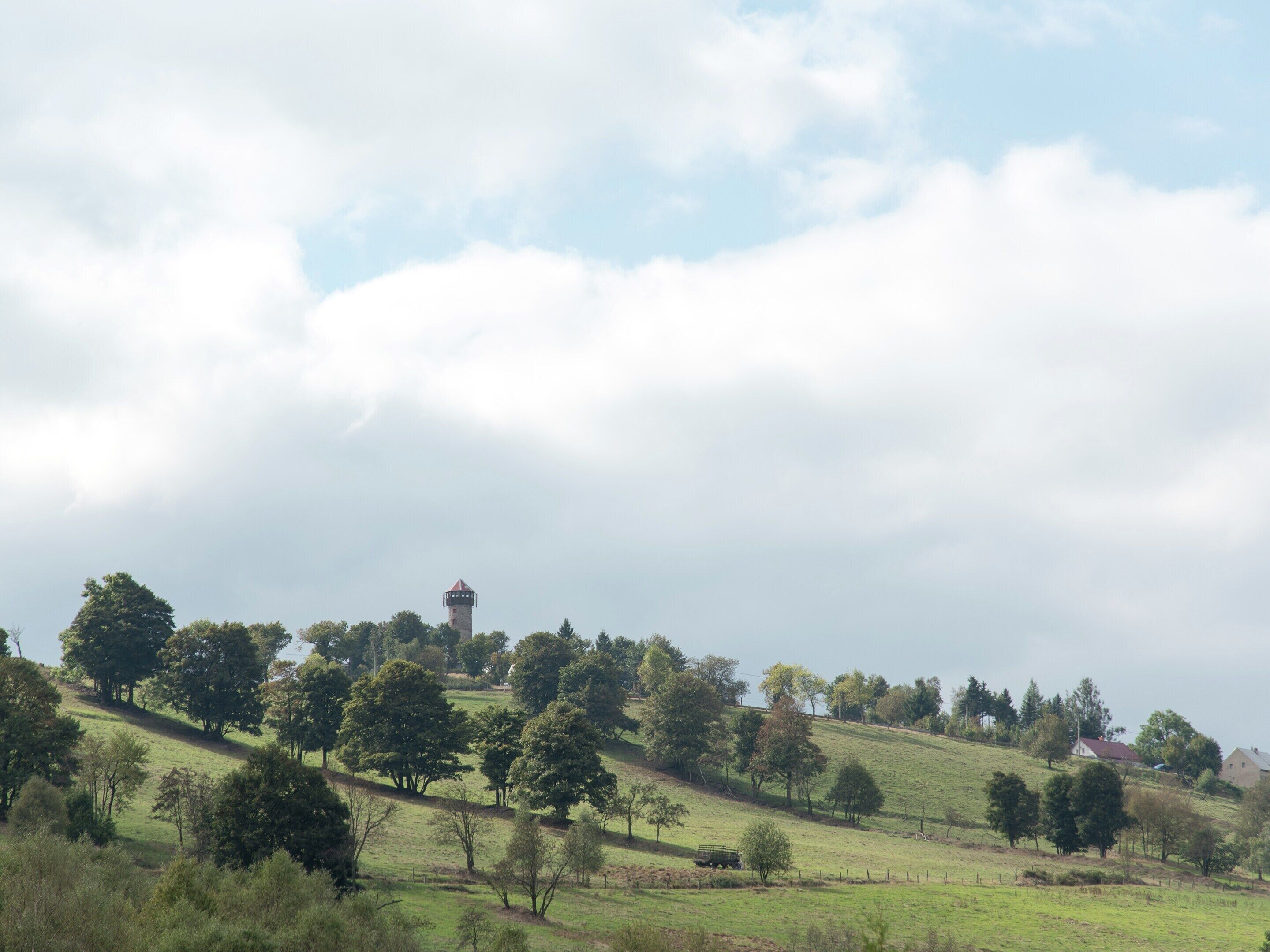 Paisaje rural con una torre, árboles y colinas onduladas.