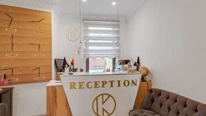 A reception area with a wooden wall displaying clocks set to different cities, a reception desk with 'RECEPTION' signage, and a brown sofa. - Apartment in Oberhausen Near a Lake (Oberhausen)