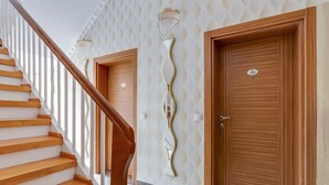 A staircase with wooden steps and a wooden handrail leading to a landing. There are two doors with numbers on them, and a wall with a wavy pattern. - Apartment in Oberhausen Near a Lake (Oberhausen)