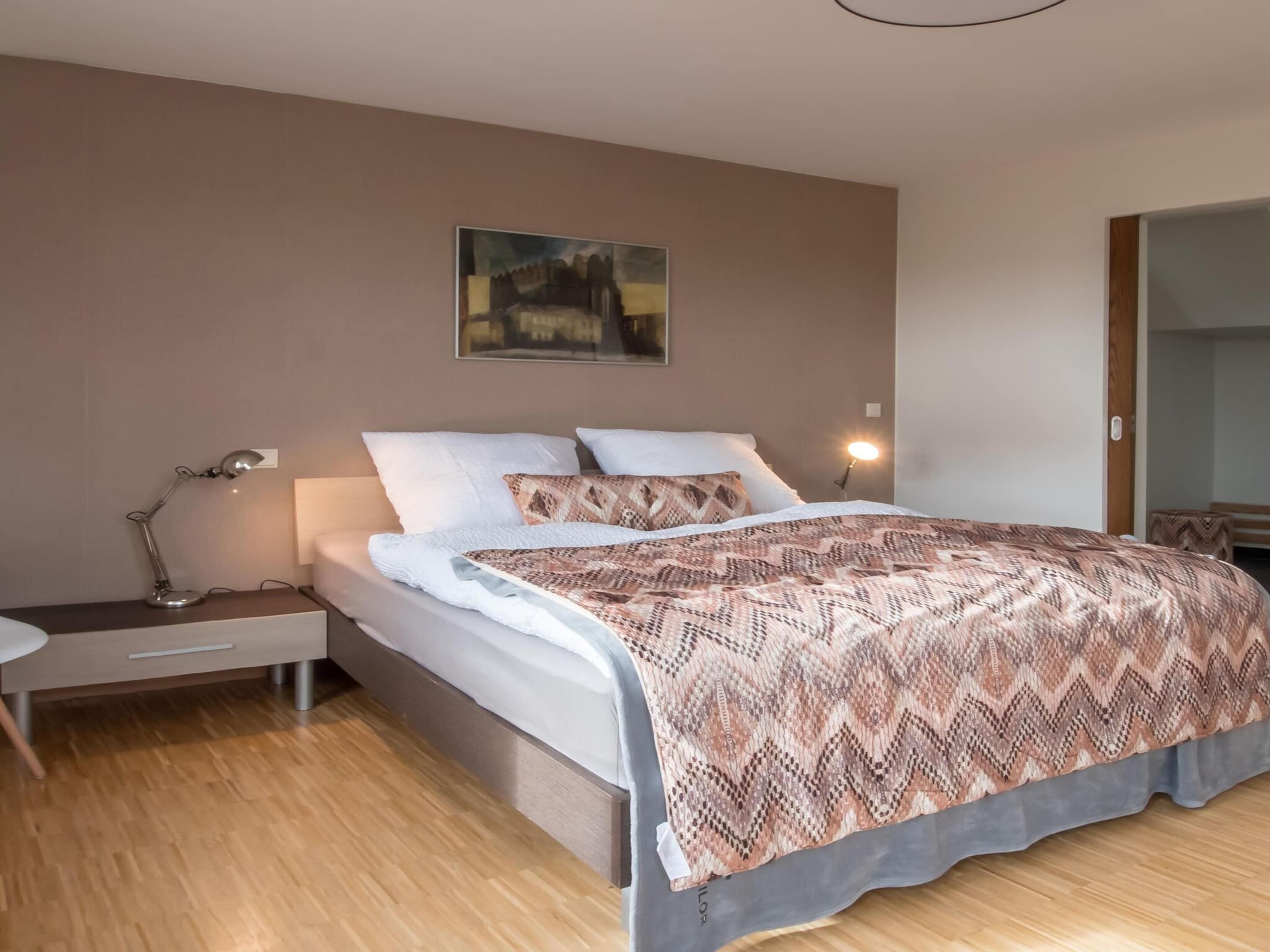 A modern bedroom with a bed, bedside table, lamp, and a painting on the wall.