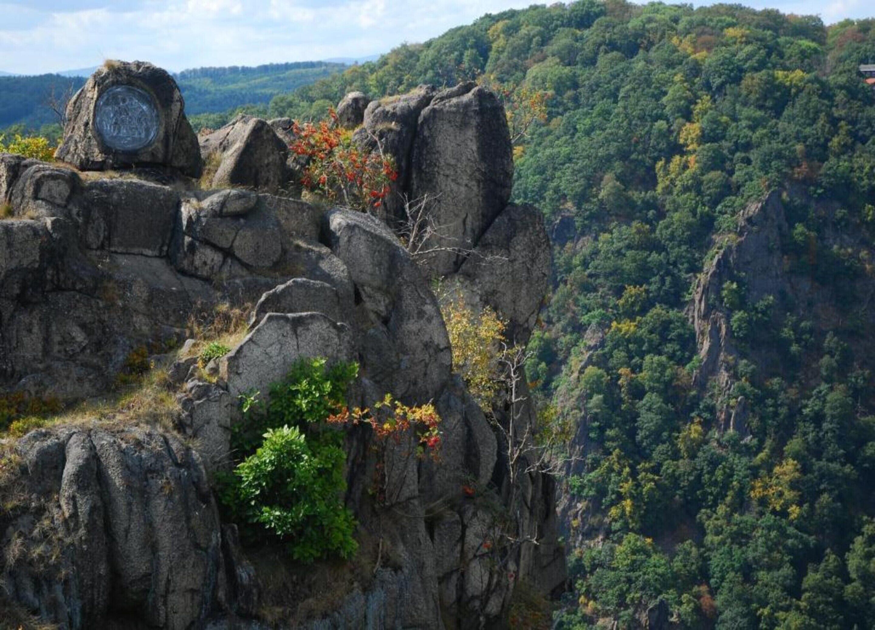 A rocky cliff with a plaque and a view of a forested valley.