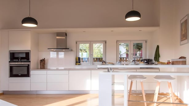 A modern kitchen with white cabinetry, a built-in oven, and a large island with bar stools. - Elegant Escape in Quedlinburg (Quedlinburg)