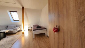 A bedroom with a loft bed, a small bedside table, a nightstand, a sofa, and a wooden wardrobe.