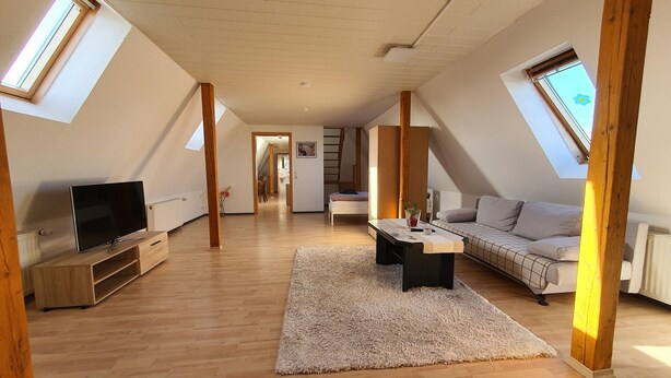 A spacious loft apartment with high ceilings, skylights, a flat-screen TV, a sofa, a coffee table, and a dining area.