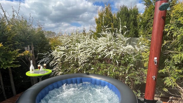 Un bain à remous extérieur installé sur une terrasse en bois, avec un poteau en bois et un robinet en métal.
