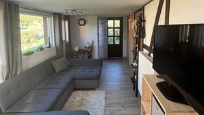 Un salon moderne avec un canapé d’angle, un téléviseur à écran plat posé sur un meuble en bois, et un coin repas comprenant une table et des chaises.