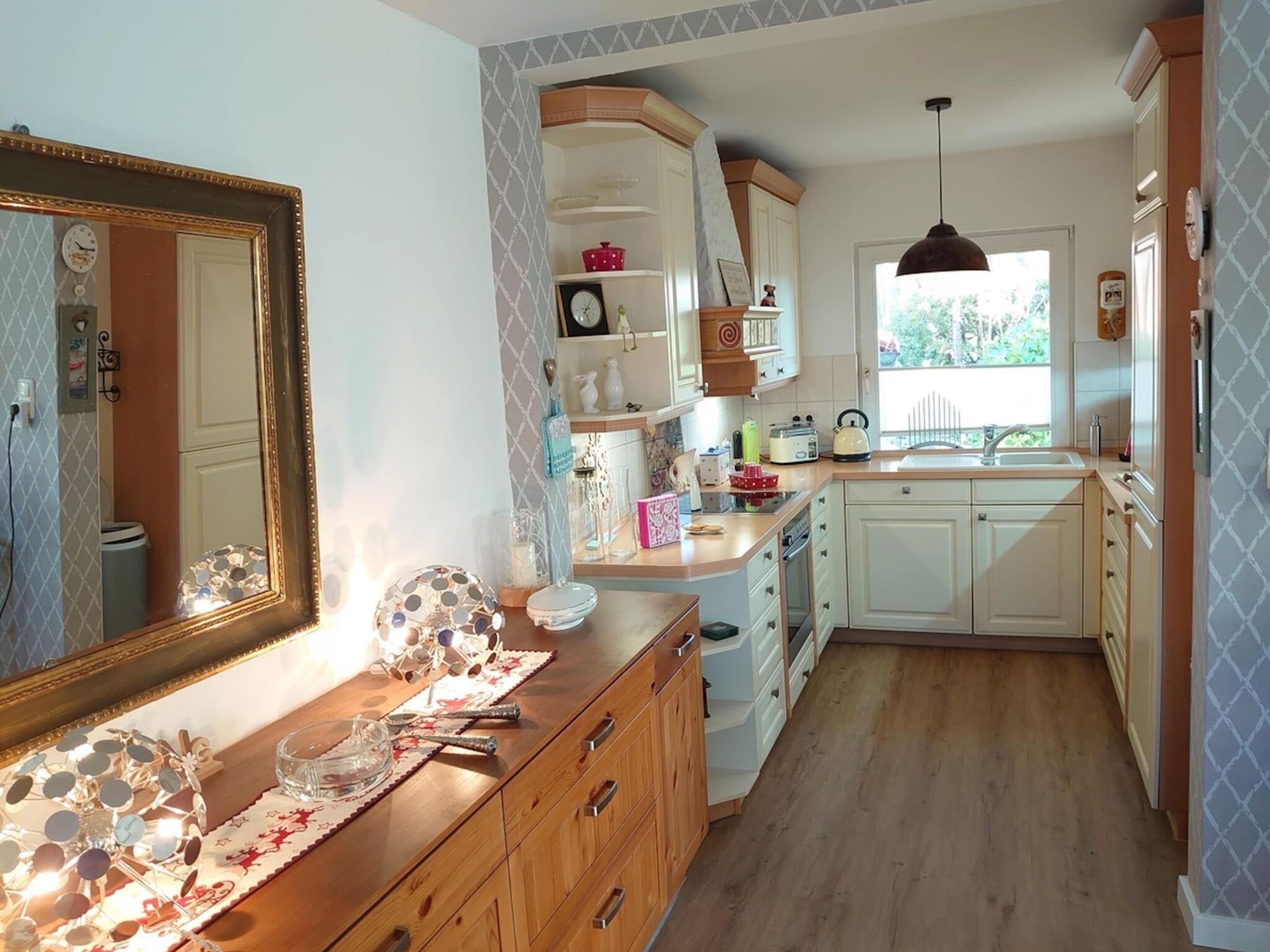 Une cuisine avec des meubles en bois, un grand miroir et une fenêtre qui laisse entrer la lumière naturelle.