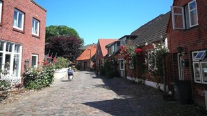 A narrow cobblestone street lined with red brick houses, each with white-framed windows and red-tiled roofs. - Wellness & Comfort Retreat (Fehmarn)