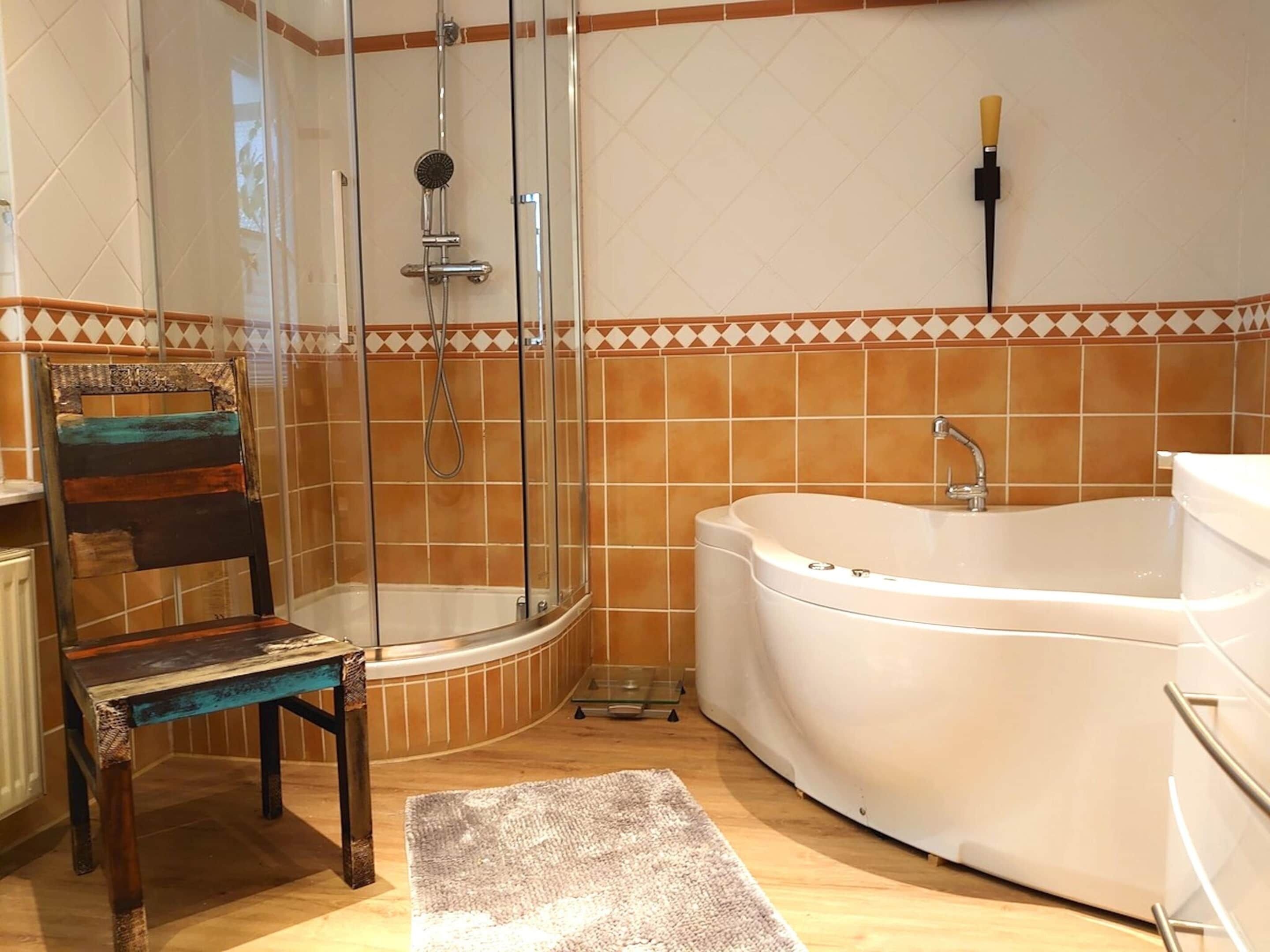 A bathroom with a glass-enclosed shower, a white bathtub, and a wooden chair.
