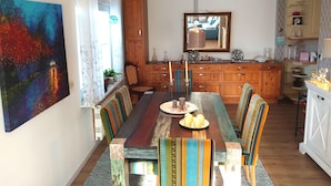 A dining area with a wooden table, colorful chairs, and a large painting on the wall. - Wellness & Comfort Retreat (Fehmarn)