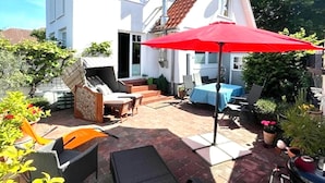 A patio area with outdoor furniture, a red umbrella, and potted plants. - Wellness & Comfort Retreat (Fehmarn)