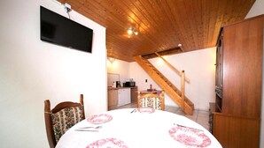 Ein Essbereich mit einem runden Tisch für vier Personen, einem an der Wand befestigten Fernseher und einer Küche im Hintergrund.