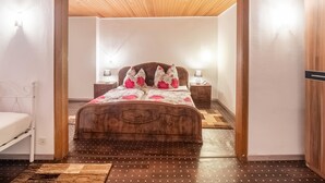 A bedroom with a wooden ceiling, a bed with floral bedding, two bedside tables with lamps, and a small nightstand with a clock. - Exceptional Holiday Flat in Kinheim (Kinheim)