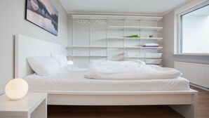 A modern bedroom with a bed, white nightstands, a wall-mounted shelving unit, and a large window. - Apartment With Terrace Near Niedersfeld Forest (Winterberg)