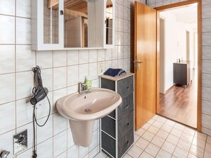 Une salle de bain moderne avec un lavabo beige, un miroir et une porte en bois donnant sur une autre pièce.