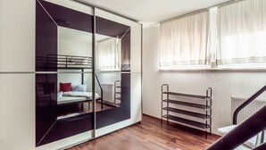 Ein Zimmer mit Etagenbett, Schiebetürenschrank, Heizkörper und einem fenster mit Vorhängen.