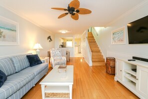A spacious living room with a sofa, coffee table, and a television. There is a staircase leading to an upper level.