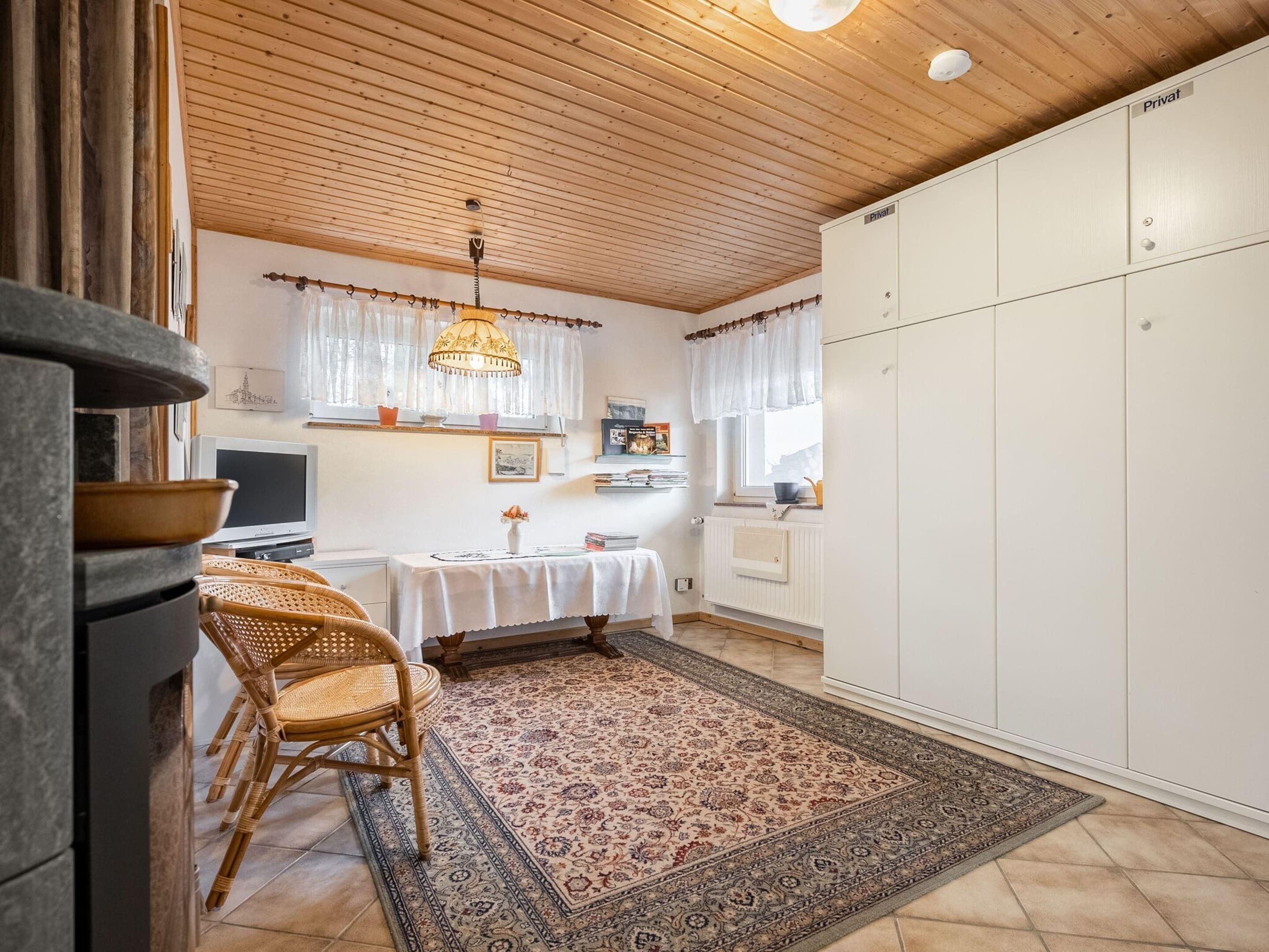 A kitchen with wooden ceiling, white cabinets, a dining table with chairs, and a patterned rug.