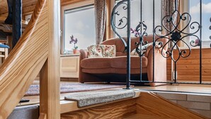 A wooden staircase with a cushioned landing, a metal railing, and a view of a living room with a sofa and a window. - Ferienhaus in Harzgerode (Harzgerode)