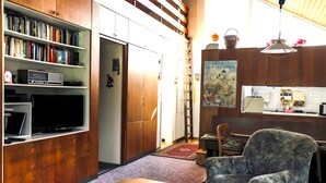 A compact living space with a bookshelf, a television, a dining area, and a chair. - Nordsee-ferienhaus mit Terrasse (Wangerland)