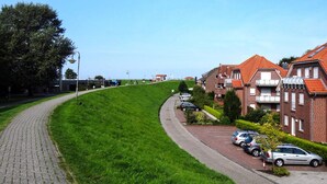 A residential street with houses, parked cars, and a paved walkway. - Nordsee-ferienhaus mit Terrasse (Wangerland)